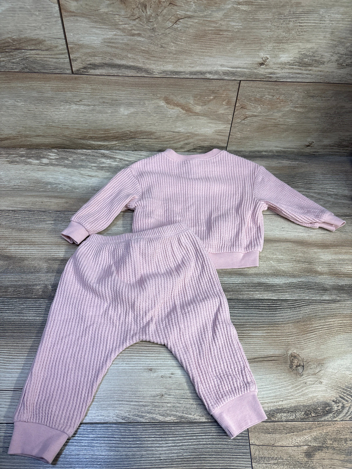 Flat lay of pink knit henley sweater and matching pants set with ribbed texture and cuffed hems on a wood plank background