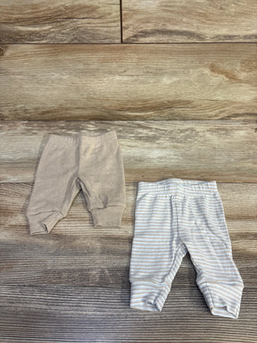 Top-down view of Just One You newborn 2-pack pants showing a solid beige pair and a beige-striped pair with elastic waists on wood background