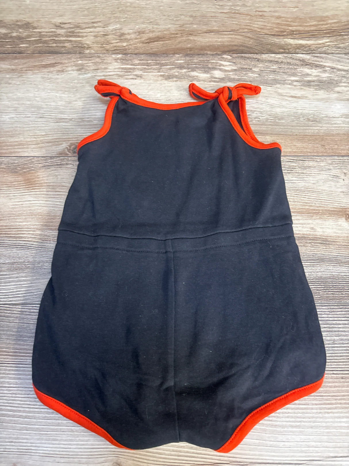Black baby romper with red trim and shoulder ties on wooden background