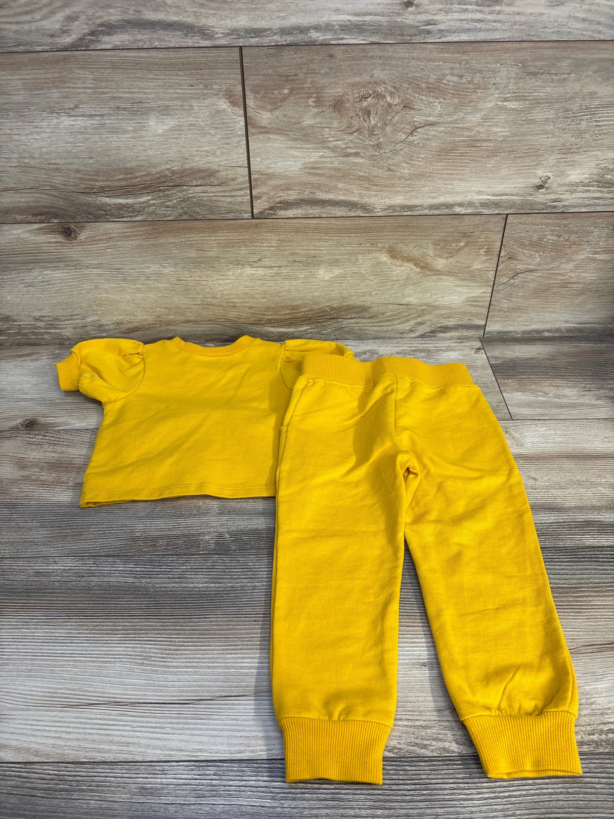 Bright yellow toddler outfit with short sleeve top and jogger pants on wood floor