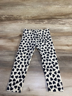Flat lay of ivory girls' leggings showing all-over black heart print and elastic waistband on light wood floor, size 2T