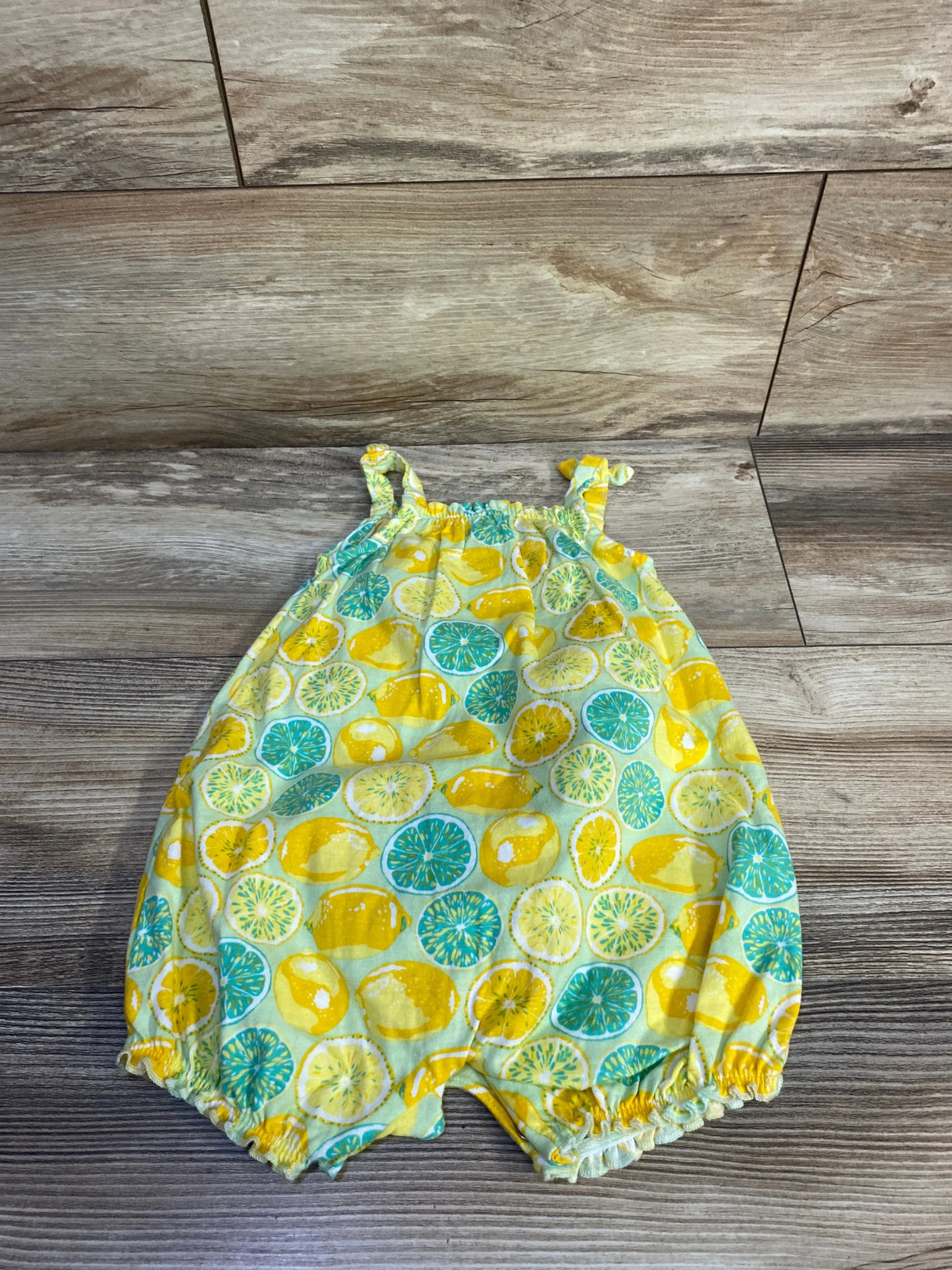 Flat lay of 12M lemon-print tank romper with gathered straps and ruffled leg openings on wood floor