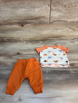 Baby outfit with orange pants and dinosaur print shirt on wood background