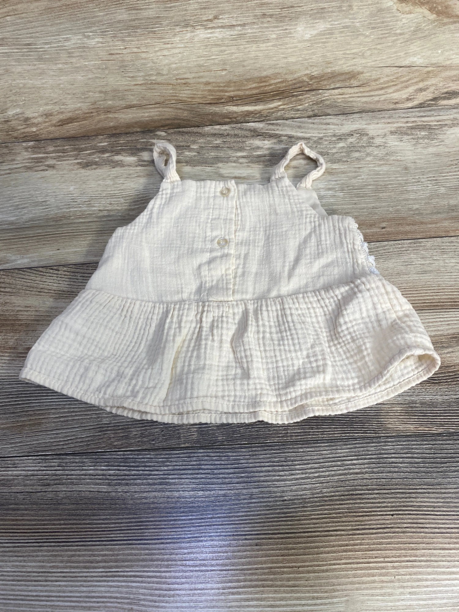Flat lay of ivory peplum tank top (24 months) showing front buttons, ruffled hem and crochet straps on wood background