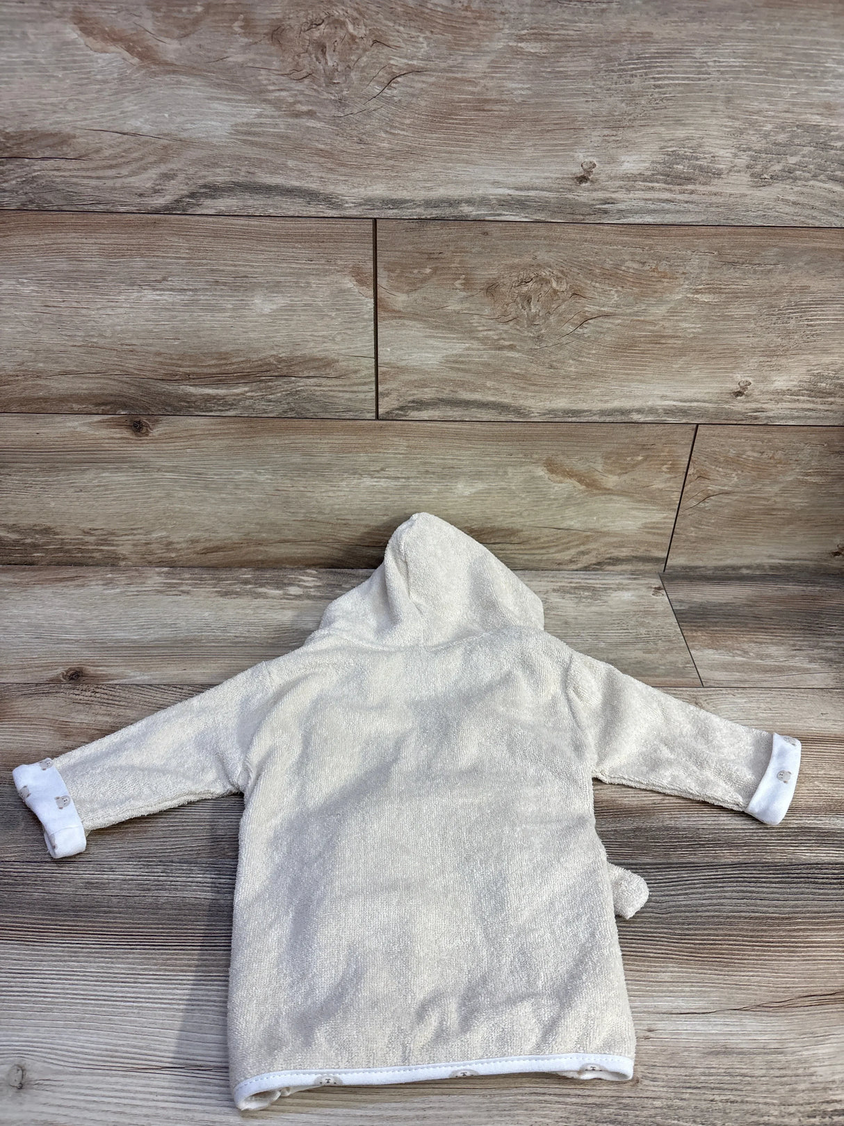 Back view of pale yellow newborn hooded terry cloth bath robe laid flat showing hood, long sleeves with rolled cuffs on wood plank background