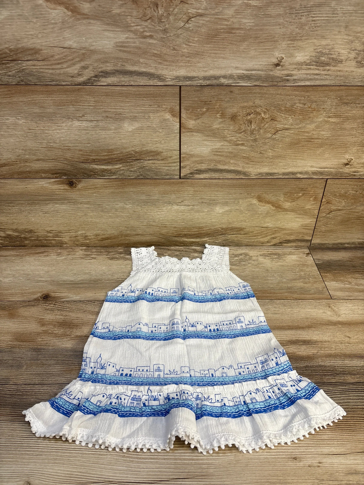 White and blue sleeveless toddler dress with cityscape print on wooden background