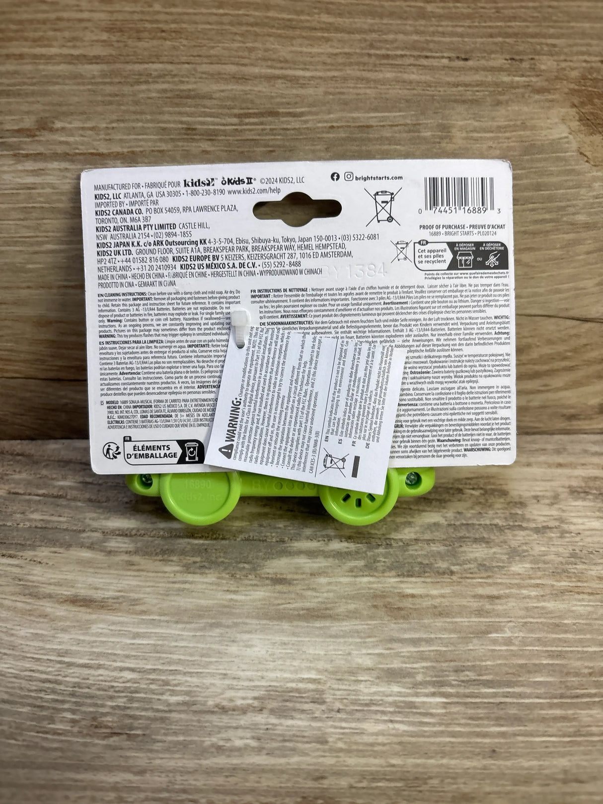 Back view of Bright Starts Safari Driver take along musical toy in packaging, showing green toy wheels on a wood surface