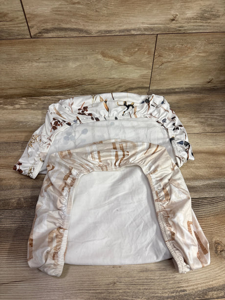 Top view of two white and tan fitted bassinet sheets showcasing elasticized edges and animal print with wood floor background