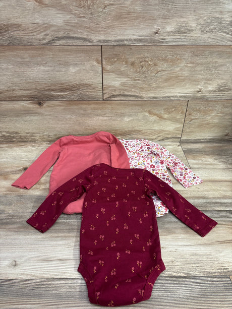 Overhead view of Just One You 3-pack long-sleeve bodysuits in red and floral patterns on a wood background