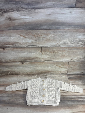 Cream knit baby cardigan sweater with wooden buttons, textured design, laid on wood floor