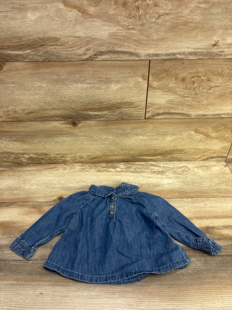 Front view of Baby Gap denim henley top in blue, size 12 to 18 months, showing ruffled collar, button placket, and cuffs on wood
