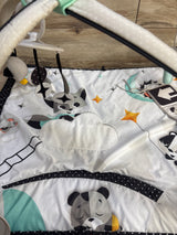Top-down view of Tiny Love Magical Tales Gymini showcasing padded black-and-white play mat with cloud applique and hanging toys on wood floor