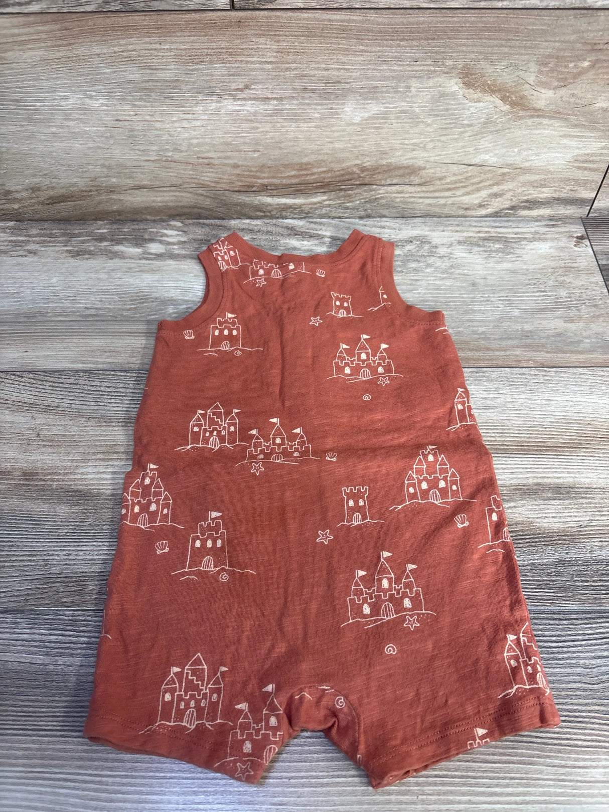 Front flat lay of brown Little Co sandcastle print romper showing sleeveless top and snap crotch on wood background