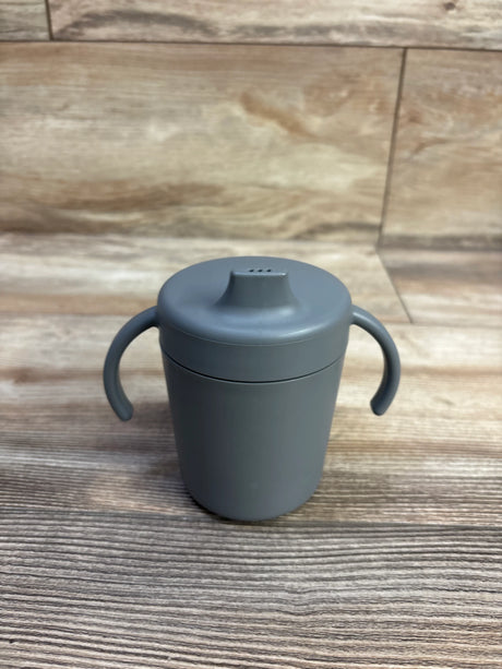 Front view of Mushie trainer sippy cup showcasing dual handles and soft spout with wooden tabletop background
