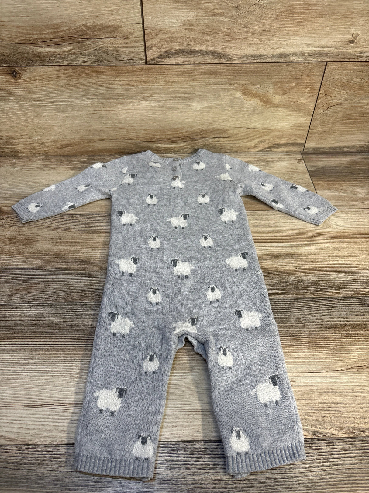 Gray knit baby romper with white sheep print, laid flat on wood background
