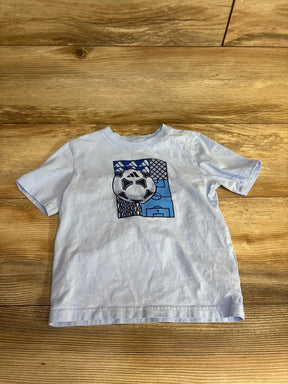 Light blue toddler T-shirt with a soccer ball and goal graphic design on wooden floor
