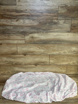 Top-down view of Peanutshell fitted crib sheet in white with pink and gray floral print showing elasticized fitted edge on wood-plank background