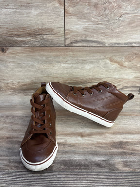 Brown leather high-top sneakers with white rubber soles on wooden floor background