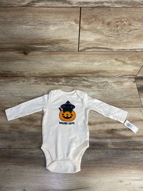 White baby onesie with Halloween pumpkin and cat design, labeled 'Wicked Cute' on wood floor.