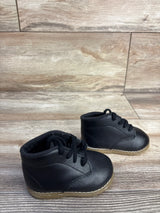 Three-quarter view of Teeny Toes Oxford first-walker shoes in black showing lace-up ankle design and tan stitched sole on wood-look background