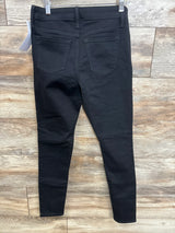 Back view of black Isabel maternity side-panel skinny jeans size XS showing back pockets and tapered legs against wood floor