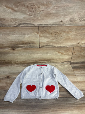 Gray children's cardigan with red heart patches on pockets, laid flat on wood floor