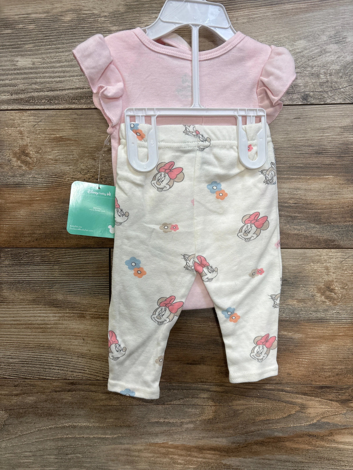 Front view of 3-piece newborn Minnie Mouse outfit: pink ruffle-sleeve bodysuit and cream Minnie-print leggings on hanger, size 0-3M