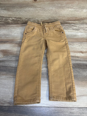 Tan kids pants with elastic waist, drawstring, and front pockets on wood floor