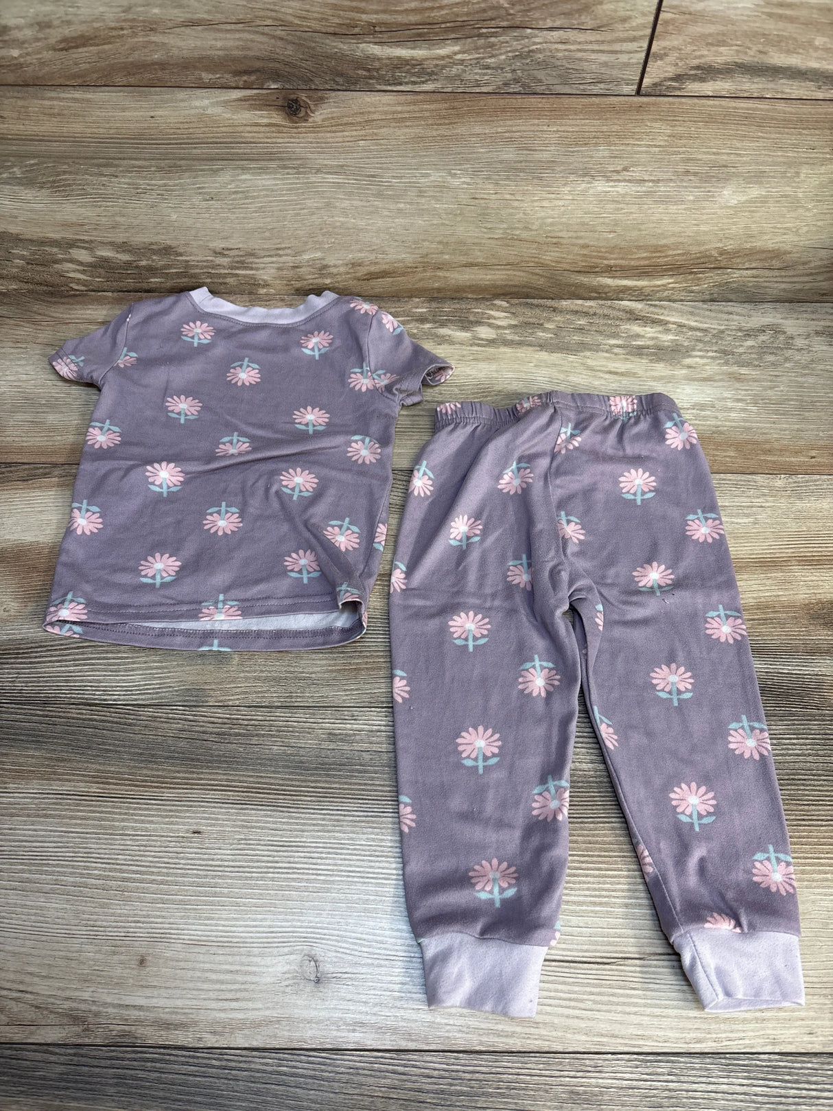 Purple floral toddler pajama set with pink flowers, short sleeve top and pants on wood floor