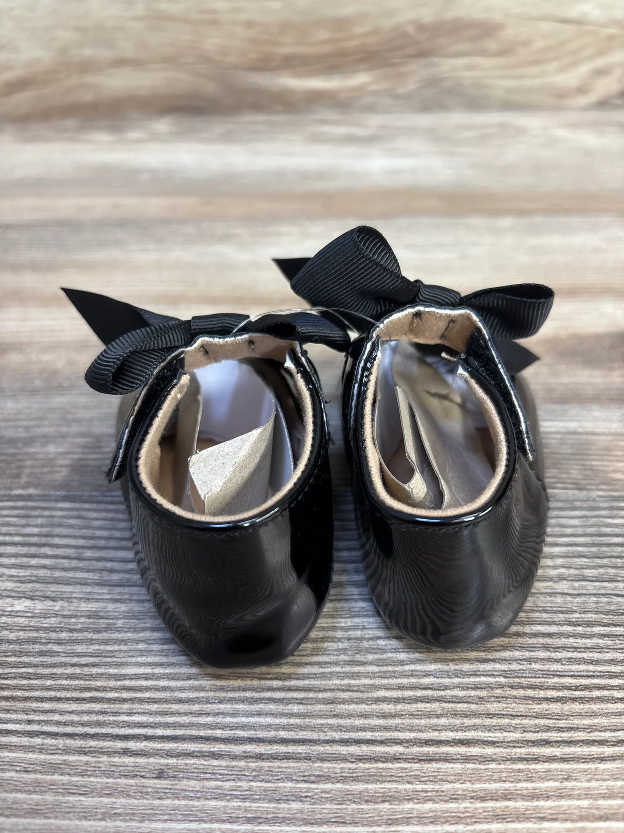 Black patent leather baby shoes with black bows on wooden background