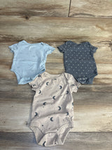 Three baby onesies with moon, star, and paper airplane prints on wood floor, ideal for newborns and infants.