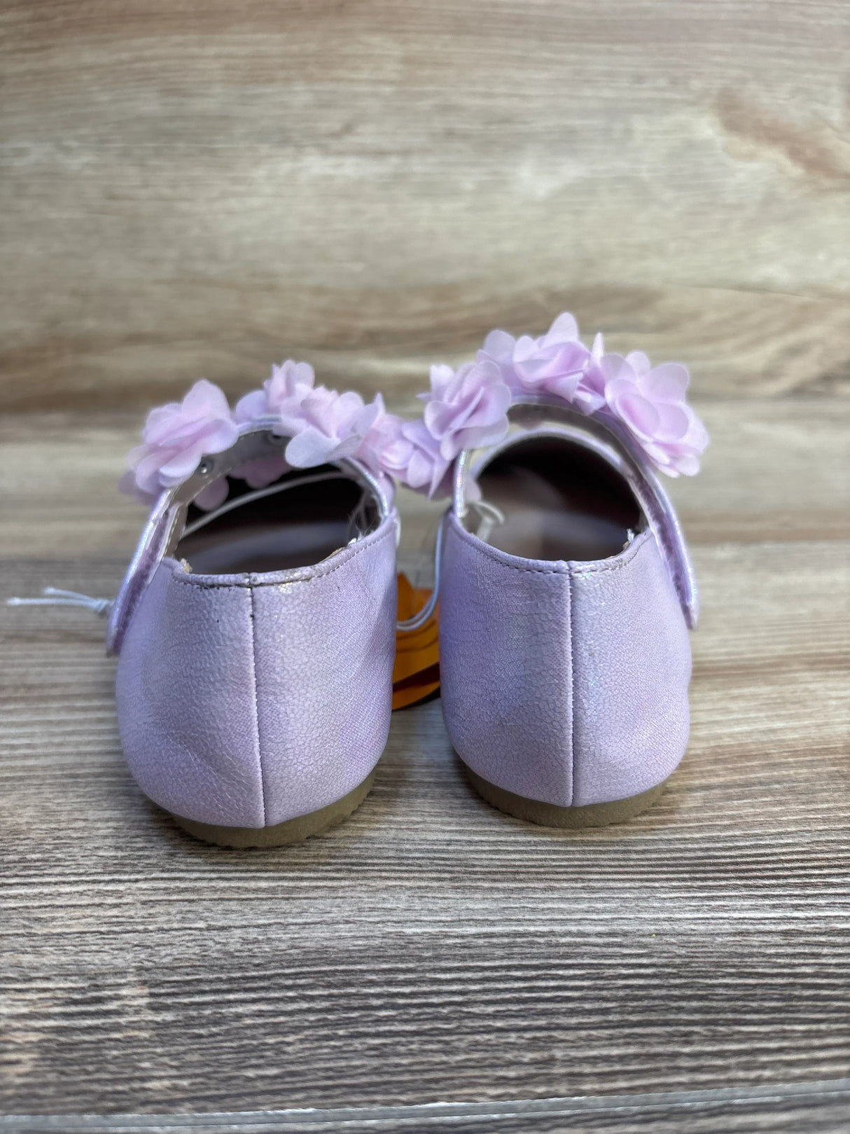 Back view of NWT Gymboree floral ballet flats in shimmery lavender showcasing pink flower strap and hangtag with wood plank floor