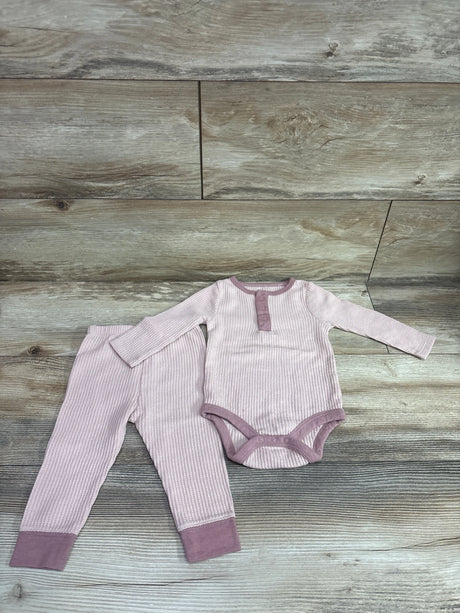 Top-down view of pink textured henley bodysuit and pants set with contrasting trim and cuffs on a wood-look background