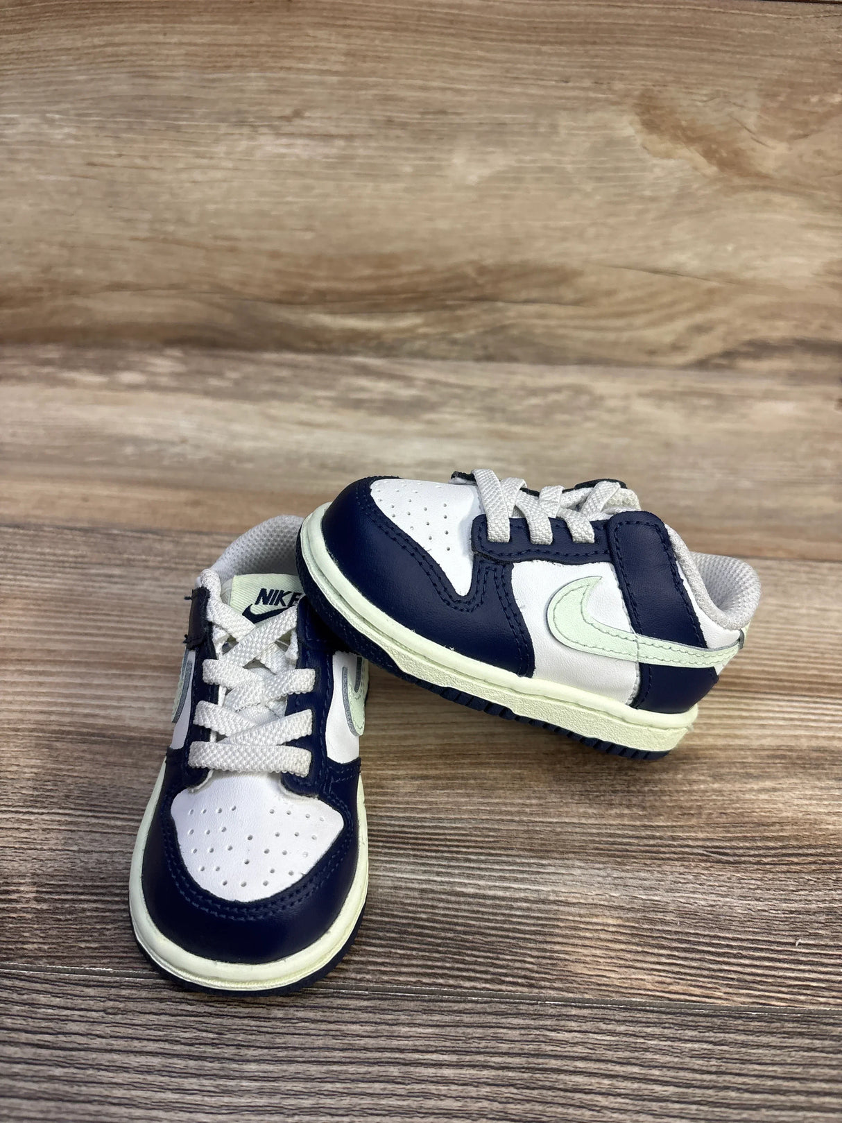 Front and side view of toddler Nike Dunk Low sneakers in midnight navy and white with pale green Swoosh, size 4C on wood background