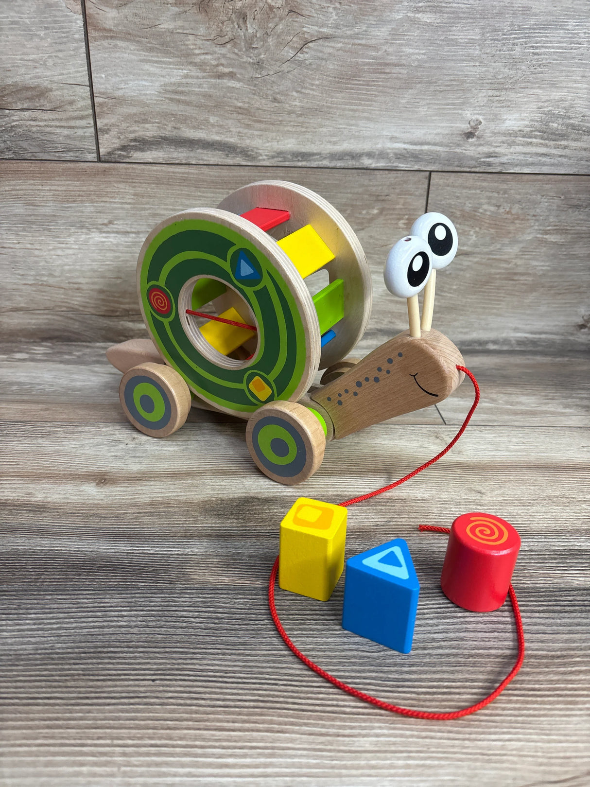 Wooden pull-along snail toy with colorful rotating shapes and large cartoon eyes on wooden floor