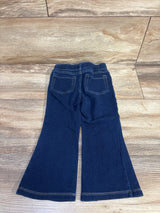 Flat-lay of blue pull-on flare jeggings showing elastic waistband, patch pockets, and flared hems on wood floor, size 2T