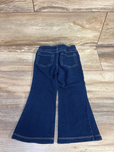 Flat-lay of blue pull-on flare jeggings showing elastic waistband, patch pockets, and flared hems on wood floor, size 2T