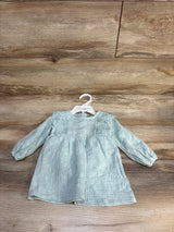 Light green long sleeve baby dress with lace detail on wooden background