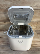 White electric sterilizer for baby bottles with open lid and metal basket on wood floor