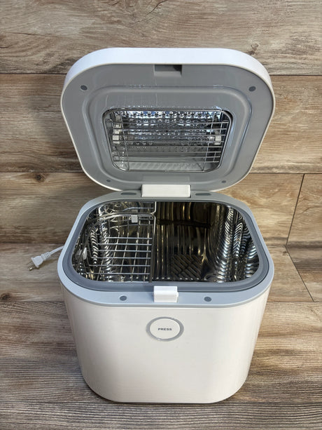 White electric sterilizer for baby bottles with open lid and metal basket on wood floor