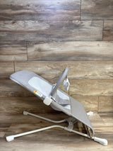 Side view of Baby Delight Highland baby bouncer showcasing pebble grey fabric, mesh center panel, toy bar with elephant plush, white metal frame on wood floor