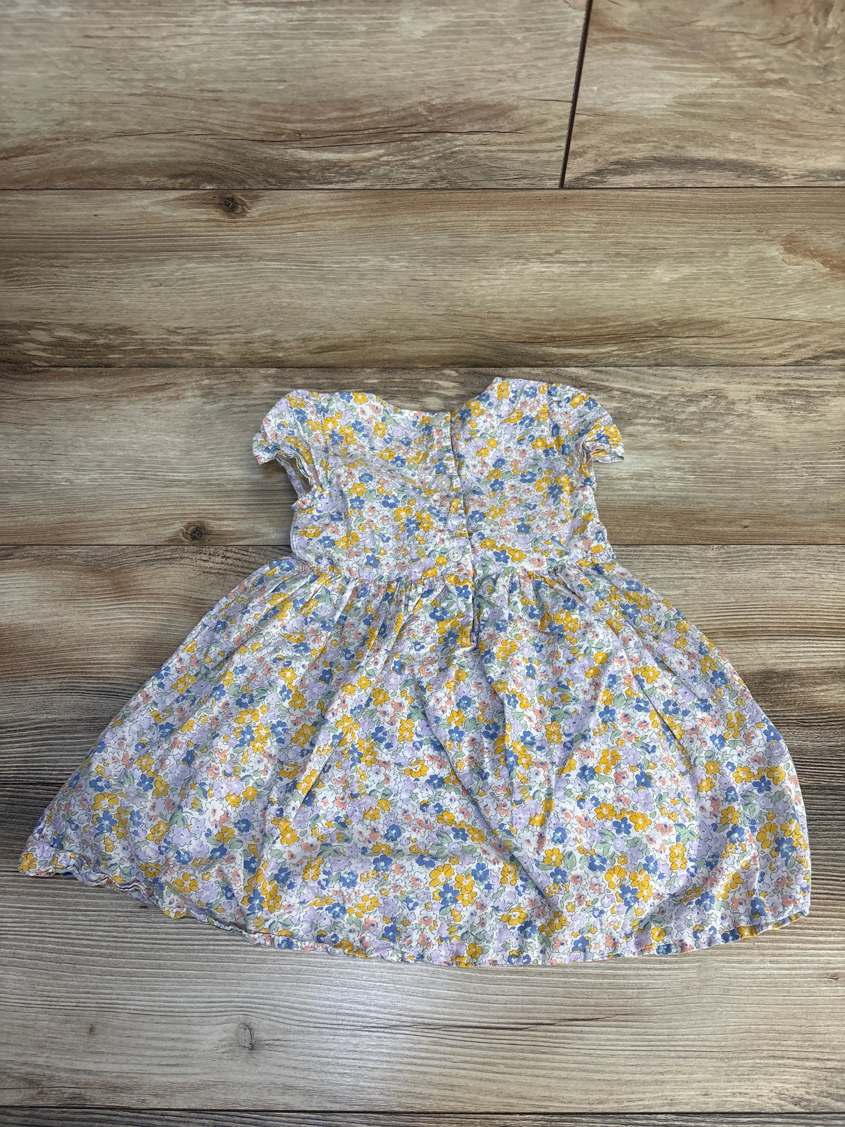 Floral print baby dress with short sleeves and buttons, laid on wood background