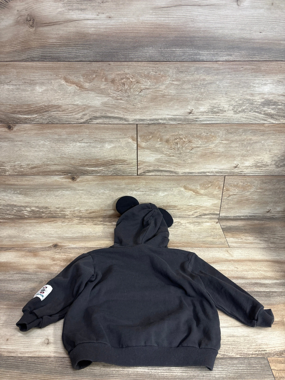 Back view of charcoal H&M x Disney Minnie Mouse toddler hoodie showing hood with Minnie ears and sleeve patch on wood floor