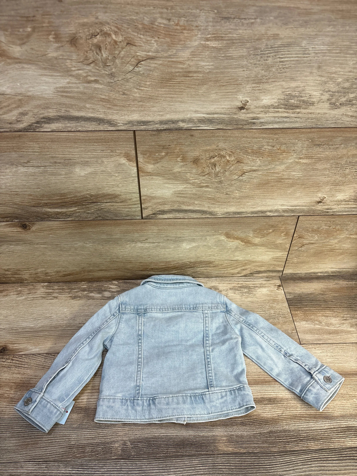 Back view of Cat & Jack light blue denim jacket, 12-month size, showing button cuffs and back yoke stitching on wood background