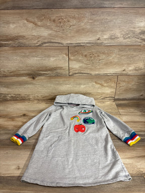 Flat lay of grey sweater dress showing rainbow cuffs and front patches including Save the World patch and red apple on wood