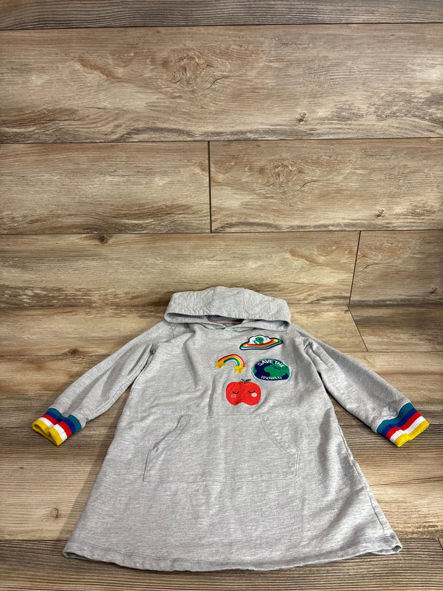 Flat lay of grey sweater dress showing rainbow cuffs and front patches including Save the World patch and red apple on wood