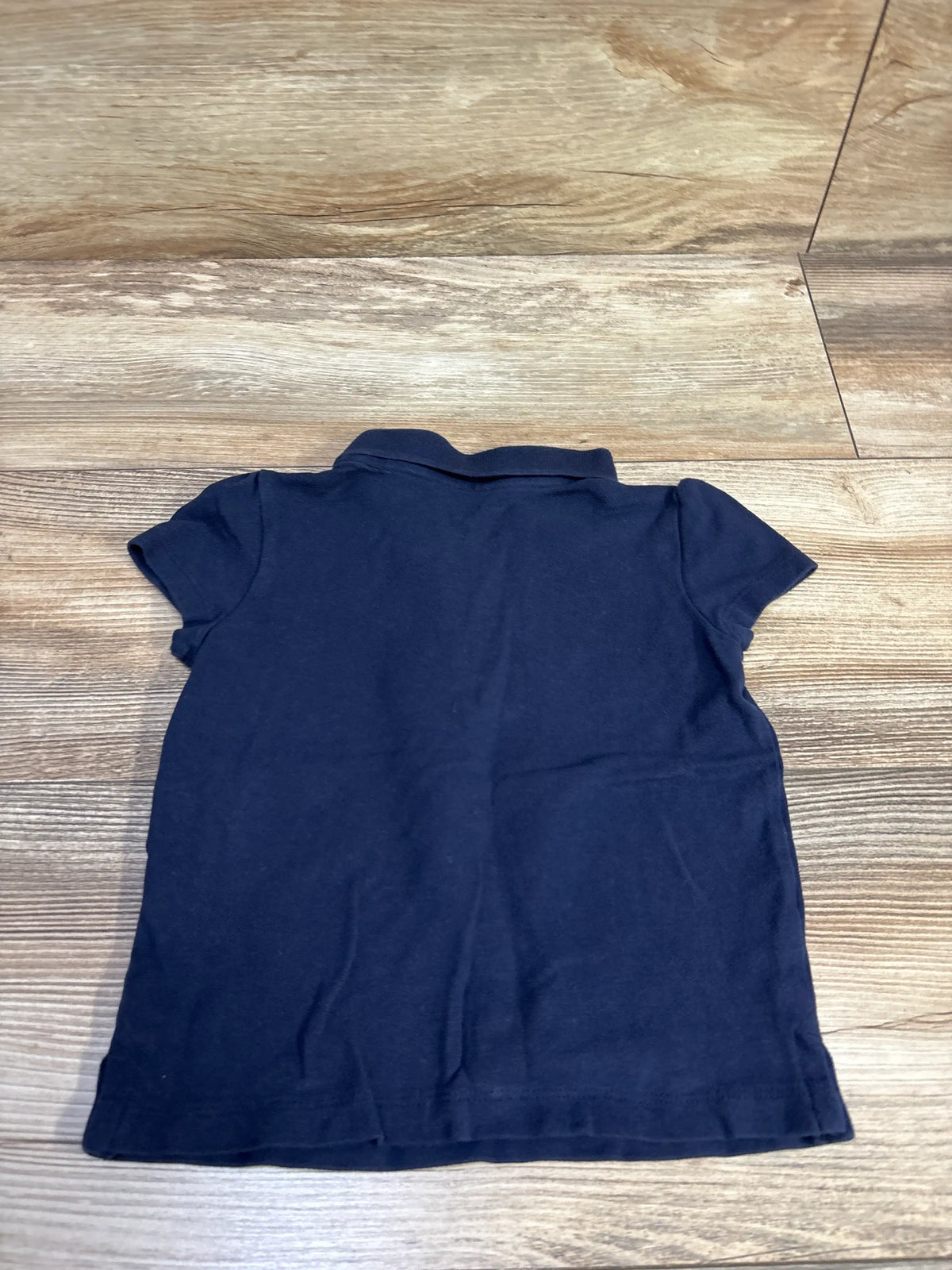 Back view of a navy blue Children's Place polo shirt for toddlers size 3T on a wood surface