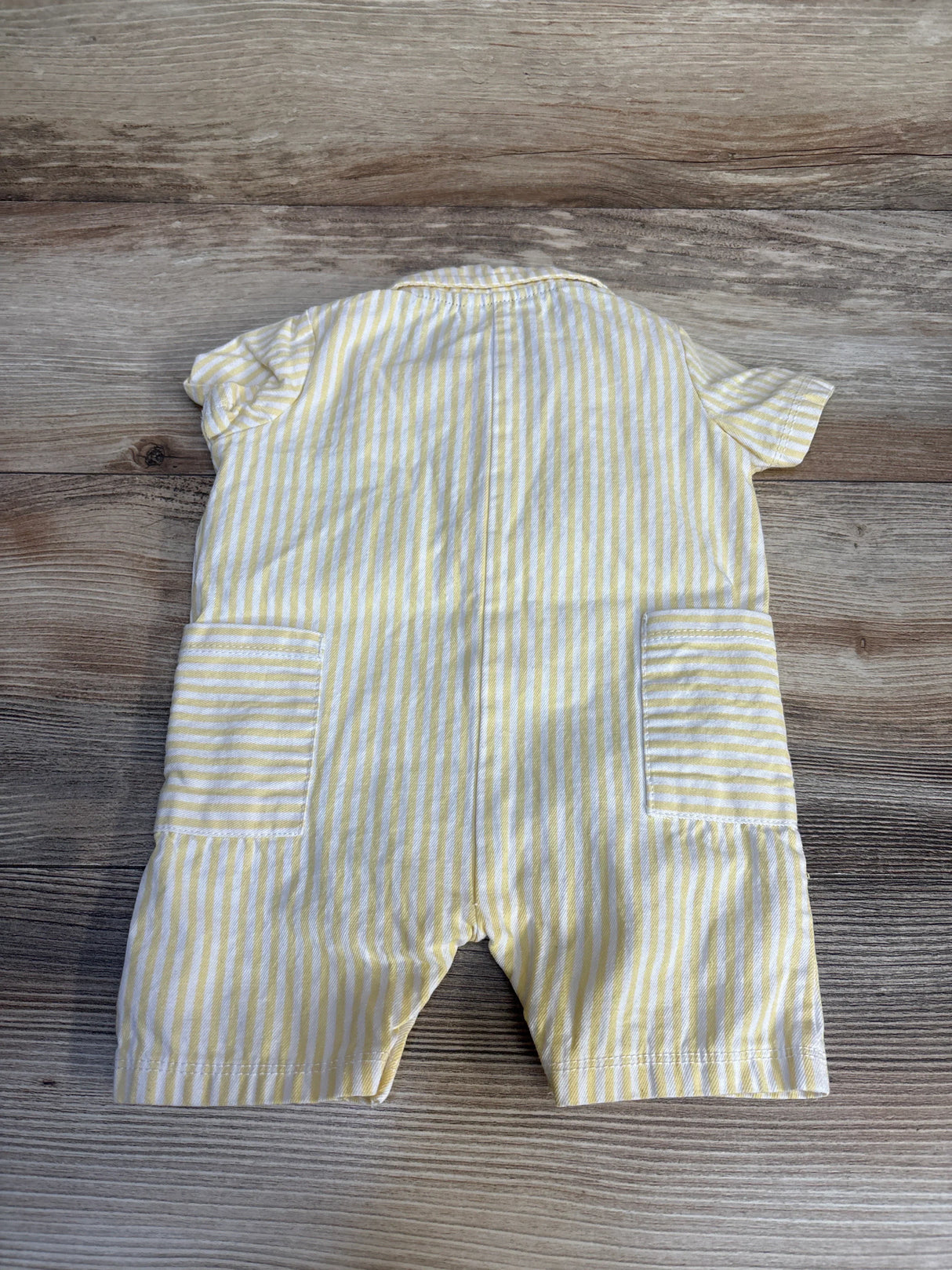 Yellow and white striped baby romper with short sleeves and back pockets on wood background