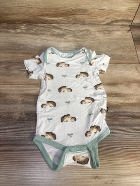 Top-down view of Kyte Baby newborn bodysuit showcasing hedgehog print, mint green trim, and snap-crotch closure on wood floor background