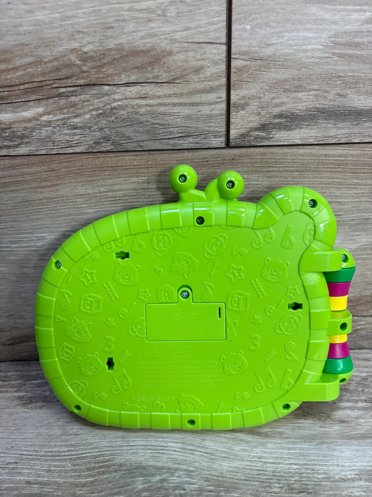 Rear of Cocomelon MacDonald Farm toy book showing green plastic back, battery compartment, embossed icons, and side rings